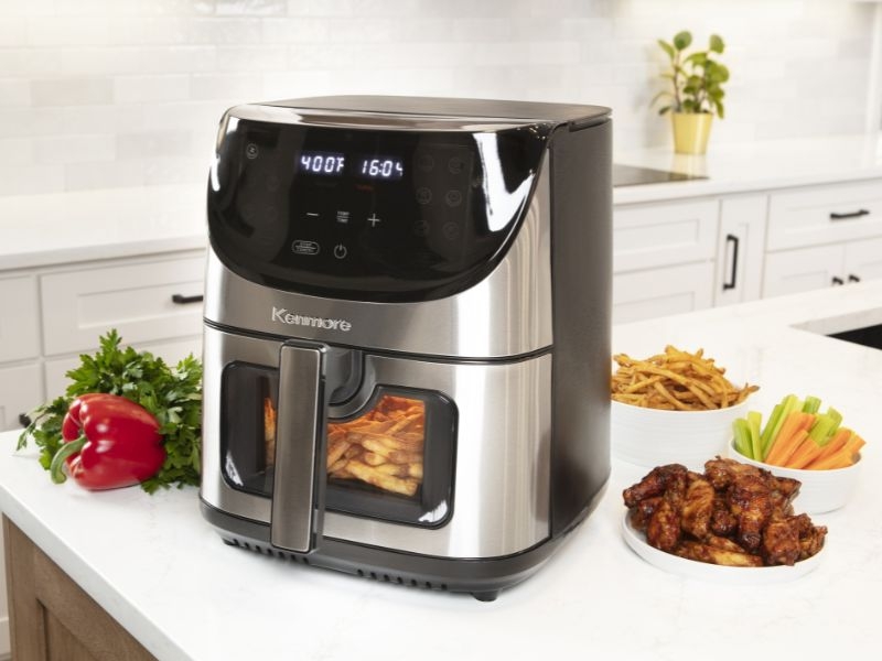 Kenmore air fryer on a kitchen counter with a variety of foods around it