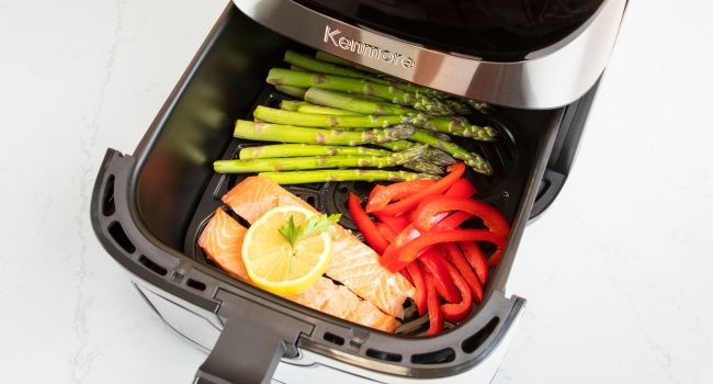 Air fryer basket pulled out with salmon, asparagus, and red pepper inside
